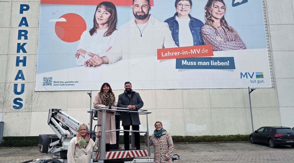 Ministerin Simone Oldenburg mit drei Lehrkräften, die Teil der Lehrerwerbekampagne sind, vor einem riesigen Plakat dieser Kampagne.