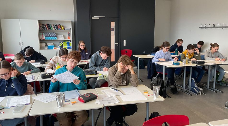 Schülerinnen und Schüler sitzen in einem Klassenraum an Einzeltischen und konzentrieren sich für ihre Mathe-Aufgaben.