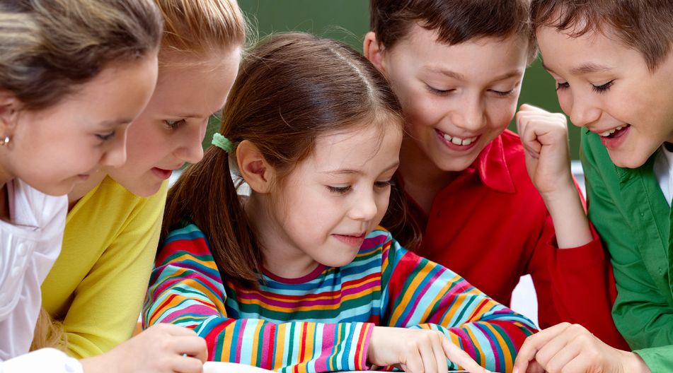 Eine Gruppe von fünf fröhlichen Grundschulkindern sitzt zusammen und liest in einem aufgeschlagenen Buch. Sie schauen gespannt auf die Seiten. Eine Gruppe von fünf fröhlichen Grundschulkindern sitzt zusammen und liest in einem aufgeschlagenen Buch. Sie schauen gespannt auf die Seiten.