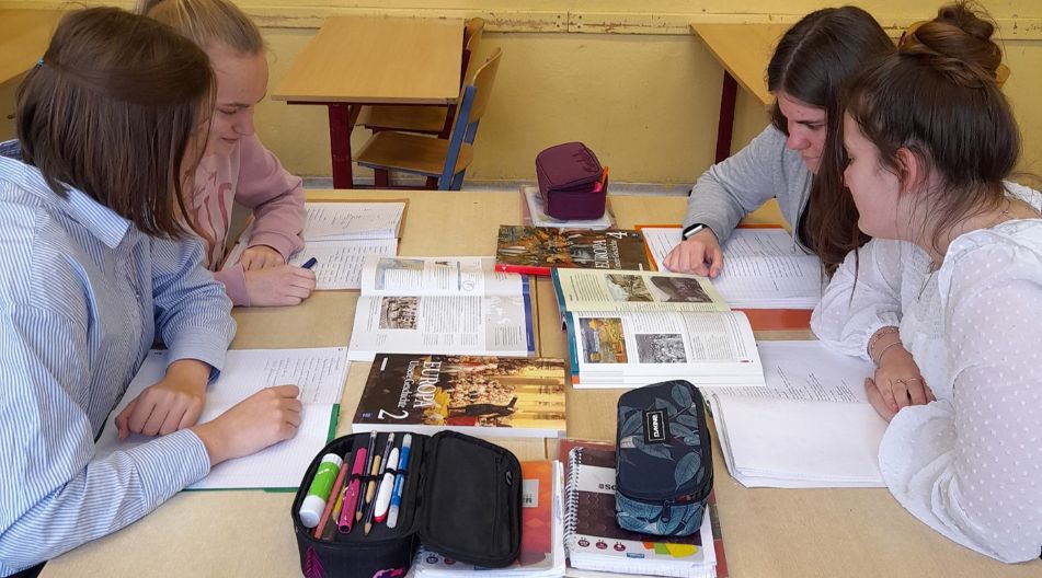 Schüler sitzen an einem Tisch und beschäftigen sich mit einem Geschichtsbuch.